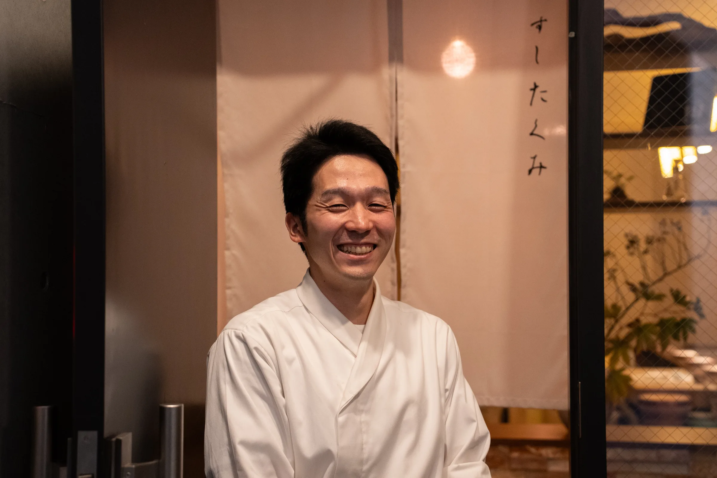 「すしたくみ」の暖簾の前で迎える大将 鈴木たくみ